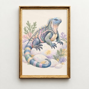 Op de afbeelding: Een ingelijste kunstdruk met een kleurrijke leguaan met blauwe, roze en gele schubben die op een groep gladde witte rotsen rust. De leguaan is omringd door gestileerde groene en paarse koraalachtige planten tegen een crèmekleurige achtergrond.
