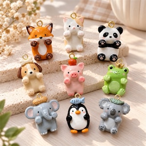 May include: A collection of nine small animal-shaped charms featuring a fox, cat, panda, dog, pig, frog, elephant, penguin, and koala. Each charm has a gold-tone metal loop at the top for hanging and a glossy, painted finish.