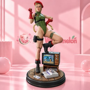 May include: A collectible figurine of a blonde character wearing a red beret, green leotard, and black boots, standing on a wooden base with a vintage television, a game console, and a controller. The television screen displays a fighting game.