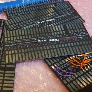 May include: Several black electronic circuit boards with silver and gold connectors and text. A blue connector is also present. Some boards have colourful wires attached. The text "THE 8 BIT MARSHED" is visible. The boards are for electronic components.