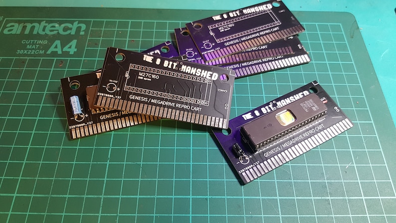 May include: Five black and purple Sega Genesis game cartridges with the text "The 8 Bit Manshed" and "Genesis/Megadrive Repro Cart" printed on them.