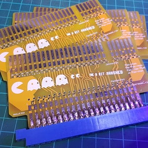 May include: A stack of six yellow circuit boards with a blue connector. The boards have a Pac-Man logo and the text "The 8 Bit Manshed" printed on them.