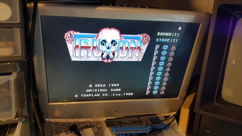 May include: A vintage arcade game screen displaying the title "TRUXION" with the game's copyright information and game stats. The screen is black with blue and white text and graphics. The game is set to round 1, stage 1.