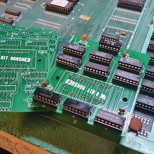 May include: A close-up of several green circuit boards with black chips and the text "THE 8 BIT MANSHED" printed on them.