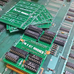 Pode incluir: Close-up de uma placa de circuito verde com vários circuitos integrados e o texto "The 8 Bit Manshed" impresso nela. Existem várias outras placas de circuito verde empilhadas em cima dela.