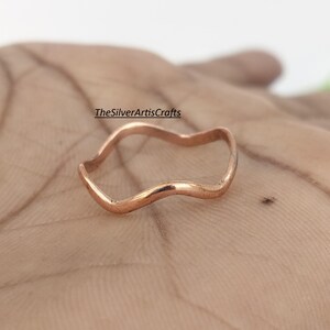 May include: A thin, wavy copper ring with a smooth, polished finish. The metal band features a continuous undulating design that curves gently around the circumference. The text TheSilverArtisCrafts is visible above the ring.