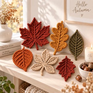 Peut inclure: Une collection de six feuilles au crochet de formes variées et aux couleurs automnales, incluant le rouge profond, le jaune doré, le vert olive, l'orange brûlé et le beige. Les feuilles présentent des mailles texturées et en relief.