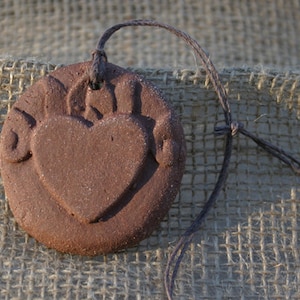 May include: A brown clay heart pendant with a cord necklace. The heart has a raised design around the edges.