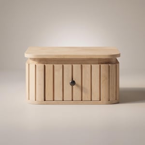 May include: A light-coloured wooden storage box with a flat top and a curved, slatted front panel. The front features a single dark, circular knob centred on the middle slat, providing a simple and functional design for organising small items.