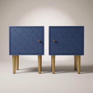 Peut inclure: Une paire de tables de chevet bleu marine carrées présentant un motif en écailles répété sur les portes avant. Chaque table est soutenue par quatre pieds fuselés en métal doré et possède un petit bouton de porte rond doré.