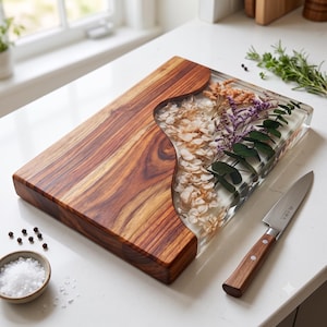 May include: A rectangular serving board featuring a natural wood section with a wavy edge and a clear resin section embedded with dried white hydrangea, purple statice, and green eucalyptus leaves, accompanied by a stainless steel paring knife.