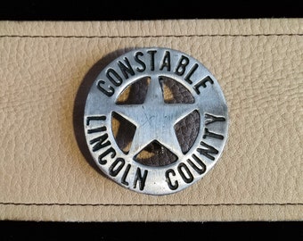 Puede incluir: Una insignia de metal plateado con las palabras "Constable Lincoln County" alrededor de una estrella de cinco puntas.