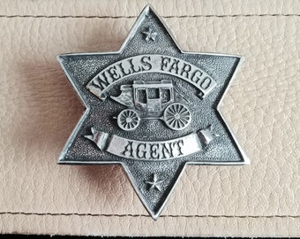 Puede incluir: Una insignia de plata en forma de estrella de seis puntas con las palabras "Wells Fargo Agent" y una representación de una diligencia.