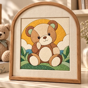 May include: A framed fabric art piece featuring a brown teddy bear sitting in a green grassy field against a yellow sun and blue sky background. The artwork is encased in a light-colored wooden arch-shaped frame with a textured cream border.