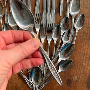 May include: A collection of silver flatware, including spoons, forks, and knives. The flatware is arranged in a fan shape and features a floral design.