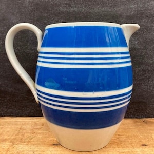 May include: A blue and white striped ceramic pitcher with a rounded body and a handle. The pitcher has a white base and a blue top with white stripes.