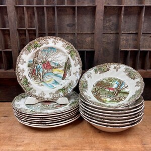 May include: A set of vintage dinnerware featuring a winter scene with a red house and trees. The set includes 10 dinner plates and 6 bowls, all in a green and brown color scheme.