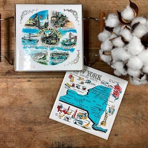 May include: Two vintage ceramic trivets with images of San Francisco and New York State. The trivets are white with blue and red accents. The San Francisco trivet features a map of the city with landmarks like the Golden Gate Bridge and Fisherman's Wharf. The New York trivet features a map of the state with the text "New York, The Empire State".