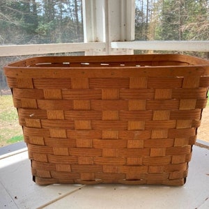 May include: A woven wooden basket with a rectangular shape. The basket is made of natural wood and has a light brown color.