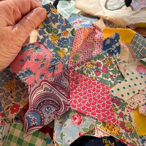 May include: A star-shaped quilt block composed of various fabric scraps featuring floral, paisley, and checkered patterns in shades of blue, pink, red, yellow, and green. The fabric pieces are stitched together with visible raw edges.
