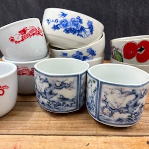 May include: A collection of eight small white ceramic teacups with blue and red floral and dragon designs.