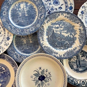 May include: A collection of antique blue and white porcelain plates. The plates feature various scenic and floral designs, including buildings, landscapes, and botanical patterns. The plates are arranged in a visually appealing, overlapping composition.