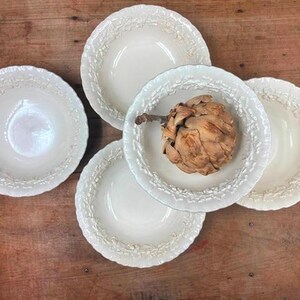 May include: Set of four white ceramic bowls with a raised floral design. The bowls are arranged in a circle with a dried artichoke in the center.