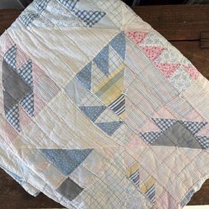 May include: A handmade quilt with a patchwork design. The quilt features a variety of fabrics in pastel colors, including pink, blue, and yellow, arranged in geometric patterns. The quilt is likely made of cotton and has a quilted texture.