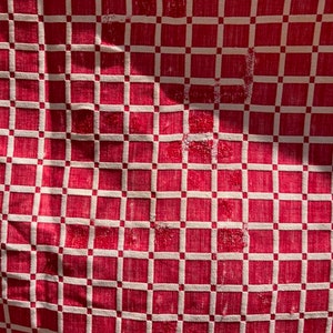 May include: Red and white checkered fabric with a woven pattern. The fabric has a slightly distressed look, with some of the threads pulled loose.