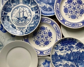 May include: A collection of eight blue and white ceramic plates with various floral and landscape designs. The plates are arranged in a circular pattern on a patterned surface.