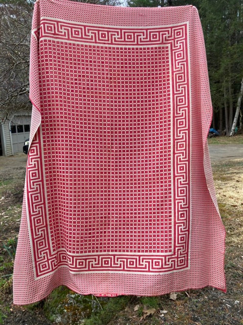 May include: A red and white picnic blanket with a geometric pattern and a Greek key border.