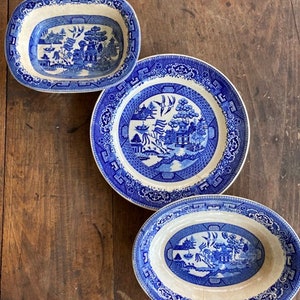 May include: Three oval blue and white porcelain dishes with a willow pattern. The dishes are arranged in a vertical stack, with the largest dish at the bottom and the smallest dish at the top.