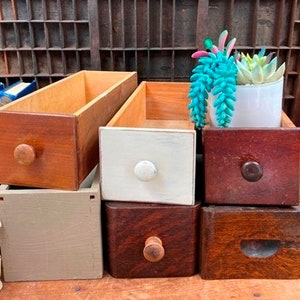 May include: Set of six wooden drawers in various colors, including natural wood, white, gray, and brown. The drawers are stacked on top of each other and have different sized knobs.