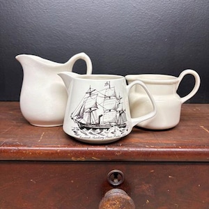 May include: A set of three ceramic mugs with a speckled, matte finish. The mugs are in shades of cream, light gray, and dark gray. Each mug has a simple, minimalist design, perfect for coffee or tea.