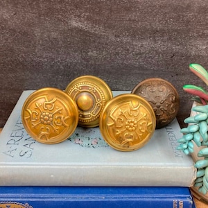 May include: Four antique brass door knobs with intricate floral designs. The knobs are arranged on top of a stack of blue and white books.
