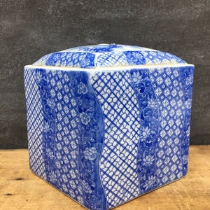 May include: Square ceramic box with a blue and white geometric pattern. The box has a lid and is decorated with a repeating design of flowers and latticework.