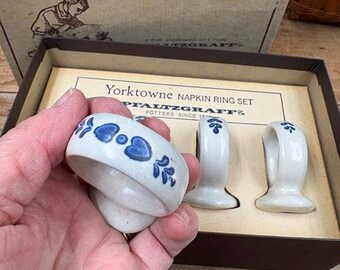 May include: A set of Pfaltzgraff Yorktowne napkin rings. The rings are white with blue floral designs. The set is in a cardboard box with the words "Yorktowne Napkin Ring Set" printed on the box.