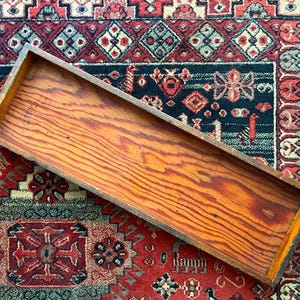 May include: A rectangular wooden tray with a natural light brown wood grain finish. The tray features four straight, solid wood sides and a flat base, showcasing a clear, visible wood texture throughout the interior and exterior surfaces.