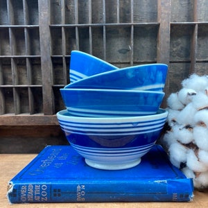 May include: Four blue and white striped ceramic bowls stacked on top of each other. The bowls are on a blue book with the title "Overheard at the Zoo" by David S.  on the cover.