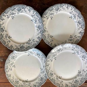 May include: Four white ceramic plates with a black and gray floral design. The plates have a scalloped edge and are arranged in a square pattern.