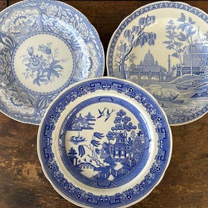 May include: Three antique blue and white decorative plates. Each plate features a different intricate design. One plate has a floral pattern, another depicts a landscape with buildings, and the third showcases a scenic oriental design.