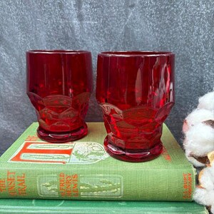 May include: Two ruby red vintage drinking glasses with a textured design. The glasses are displayed on top of two green books. The background is a gray chalkboard.