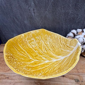 May include: A yellow ceramic leaf-shaped bowl with detailed veining. The bowl has a textured surface and a glossy finish. The bowl is a decorative piece, suitable for serving or display.