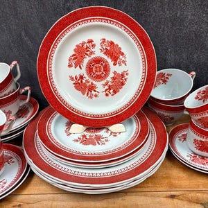 May include: A collection of red and white porcelain dishes, including plates, saucers, and teacups. The plates and cups feature a floral design with a red border. The set is arranged on a wooden surface.