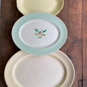 May include: Three oval ceramic serving platters in different sizes. The largest platter is white with a green rim, the middle platter is white with a green rim and a floral design, and the smallest platter is yellow.
