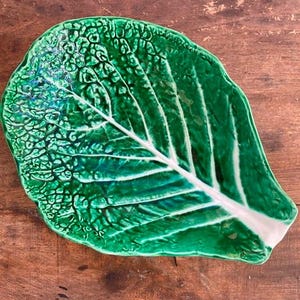 May include: A green ceramic serving dish shaped like a cabbage leaf. The dish has a white center and a green outer edge.