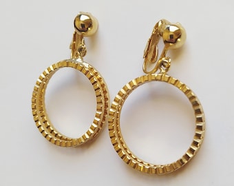 Könnte beinhalten: Ein Paar goldene Ohrclips mit einem Doppelkreis-Design. Die Kreise sind strukturiert und haben einen leicht erhöhten Rand.