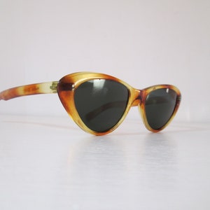 Puede incluir: Gafas de sol vintage de ojo de gato con un patr&oacute;n de carey. Las monturas son &aacute;mbar y marr&oacute;n, con lentes oscuras. Las patillas de las gafas son de un &aacute;mbar m&aacute;s claro.