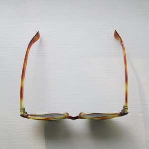 Puede incluir: Gafas con estampado de carey y lentes oscuras. Las monturas presentan una paleta de colores c&aacute;lidos en &aacute;mbar, marr&oacute;n y amarillo. Las gafas est&aacute;n sobre un fondo blanco, con una sombra proyectada a un lado.