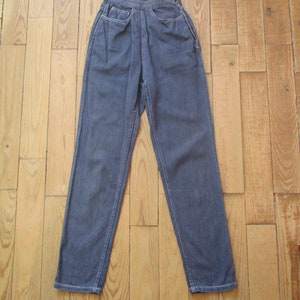 May include: Dark blue denim pants with a high waist and straight leg. The pants have two front pockets and a button and zipper closure. The stitching is white. The pants are displayed on a wooden surface.
